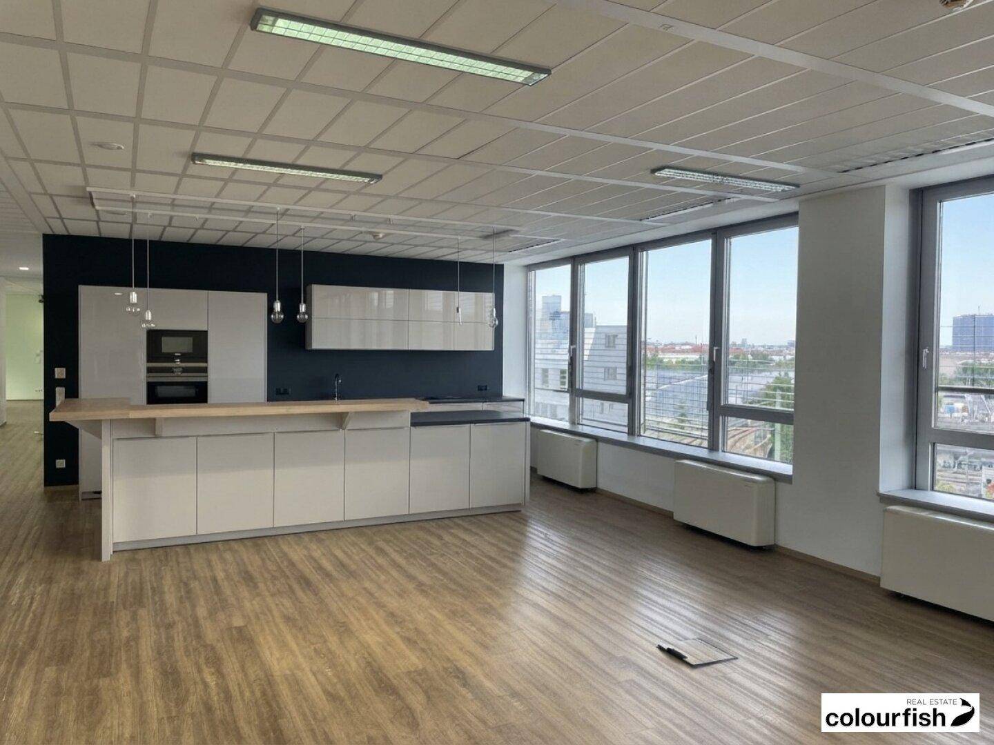 Moderner Bürobereich mit integrierter Küche, Holzboden und großen Fenstern mit Weitblick.