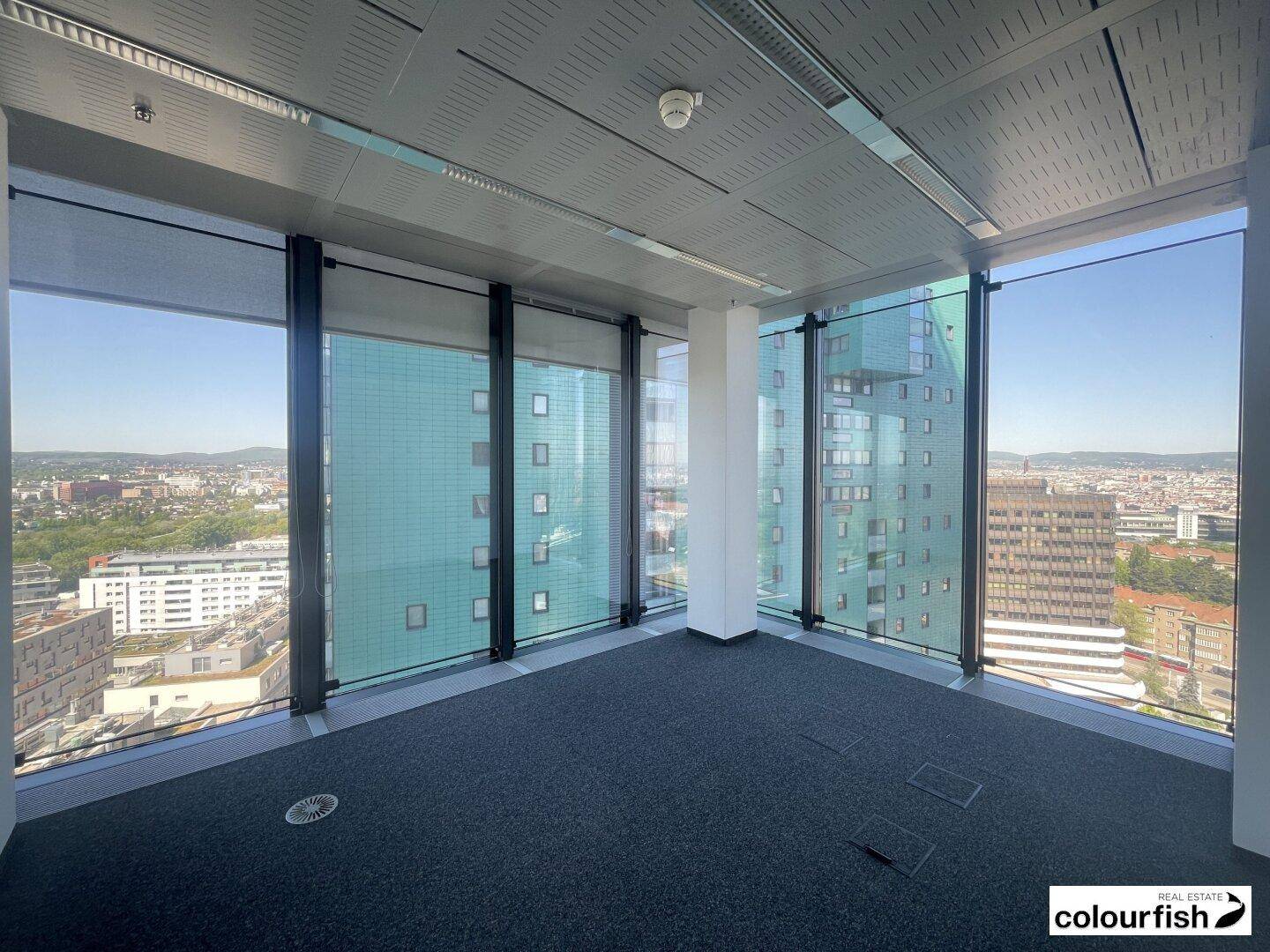 Helle Büroecke mit raumhohen Fenstern, die einen Blick auf die umliegenden Gebäude und die Stadtlandschaft ermöglichen.