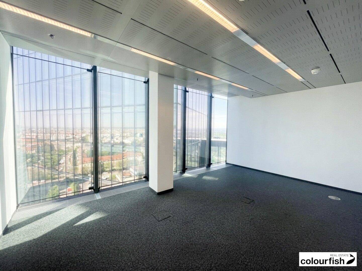 Leerer Büroraum mit großen Fenstern, die einen weiten Blick über die Stadt bieten und viel Tageslicht hereinlassen.