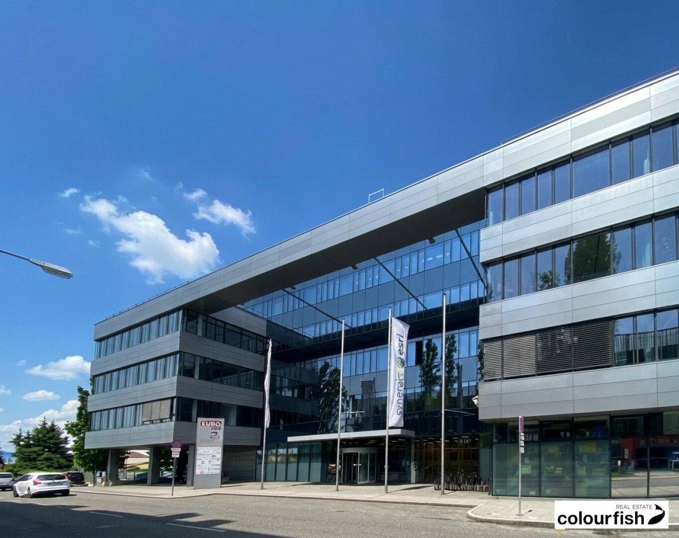 Modernes Bürogebäude mit Glasfassade und klarem blauen Himmel an einem sonnigen Tag.