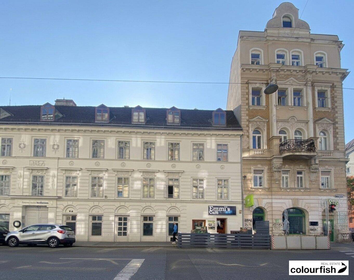Historische Gebäude mit klassischer Architektur und einem kleinen Balkon an einer belebten Straße.
