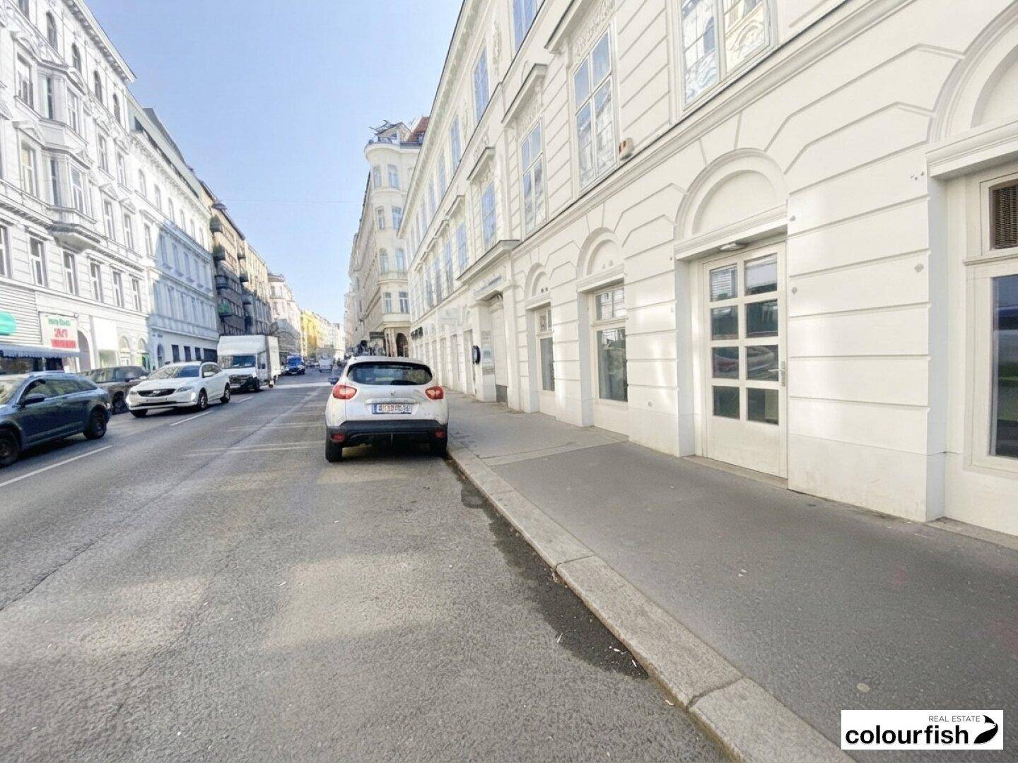 Blick auf die Straßenseite eines Gebäudes mit großen Fenstern und Türen im Erdgeschoss.