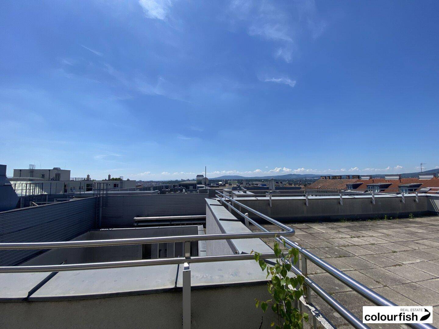 Dachterrasse mit weitem Blick über die Stadt und die entfernten Berge unter blauem Himmel.