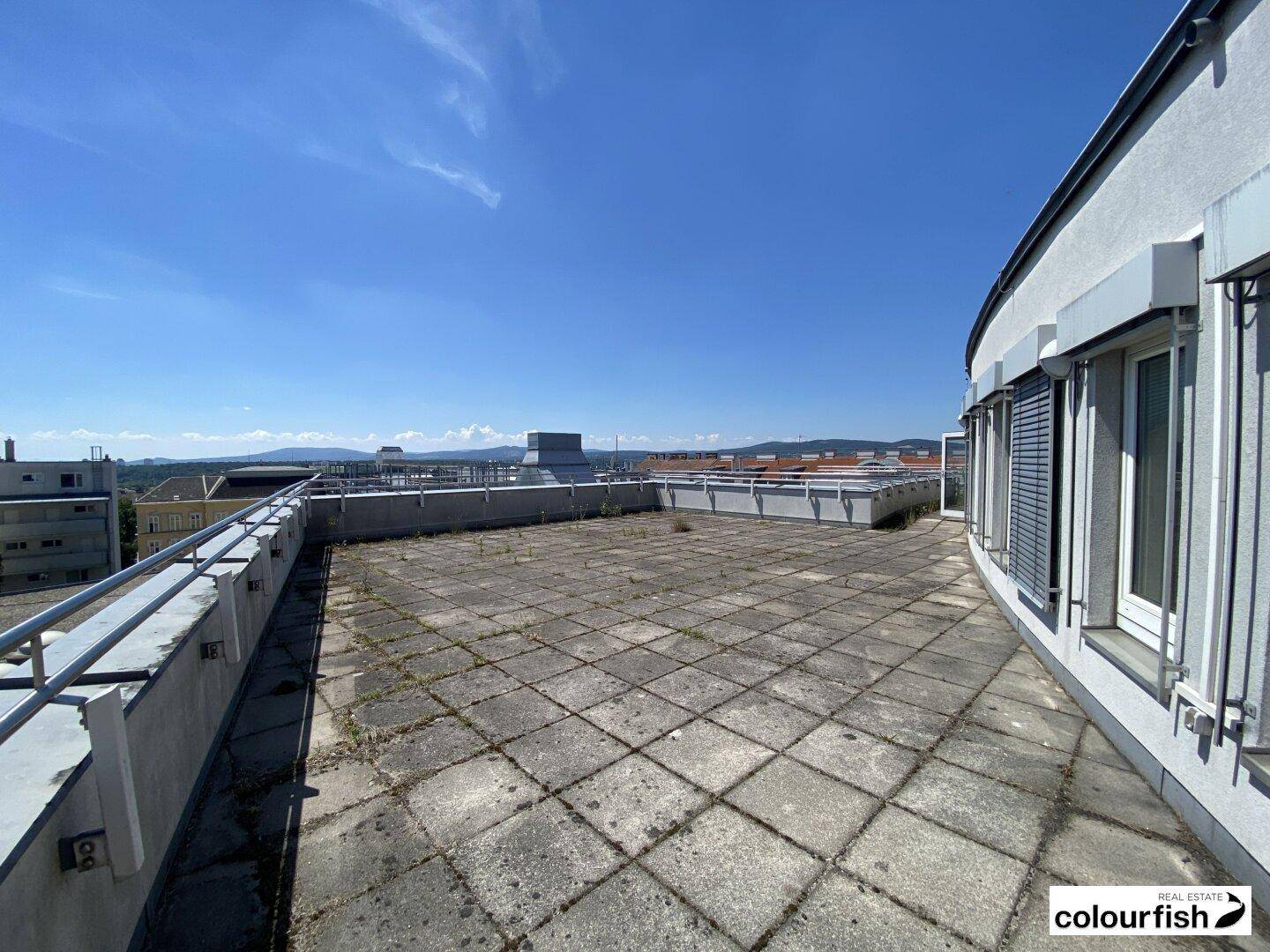 Weitläufige Dachterrasse mit Metallgeländer und Panoramablick über die Stadt und die Umgebung.