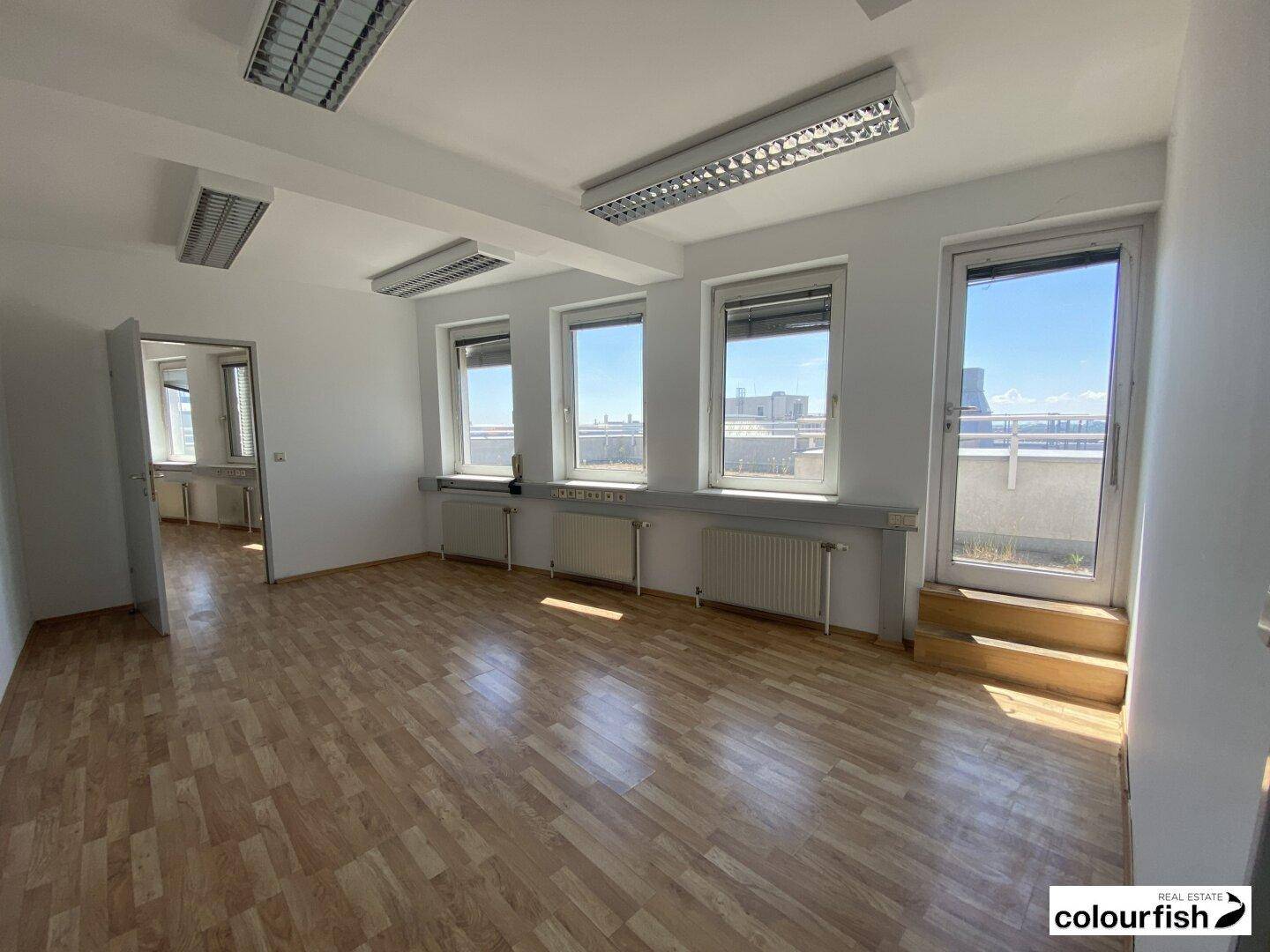 Heller Büroraum mit Holzparkettboden und direktem Zugang zur Dachterrasse durch eine Glastür.