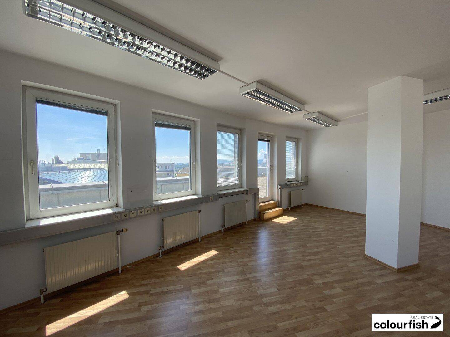 Geräumiger Büroraum mit Holzparkettboden und Zugang zu einer Außenterrasse, hell und funktional.
