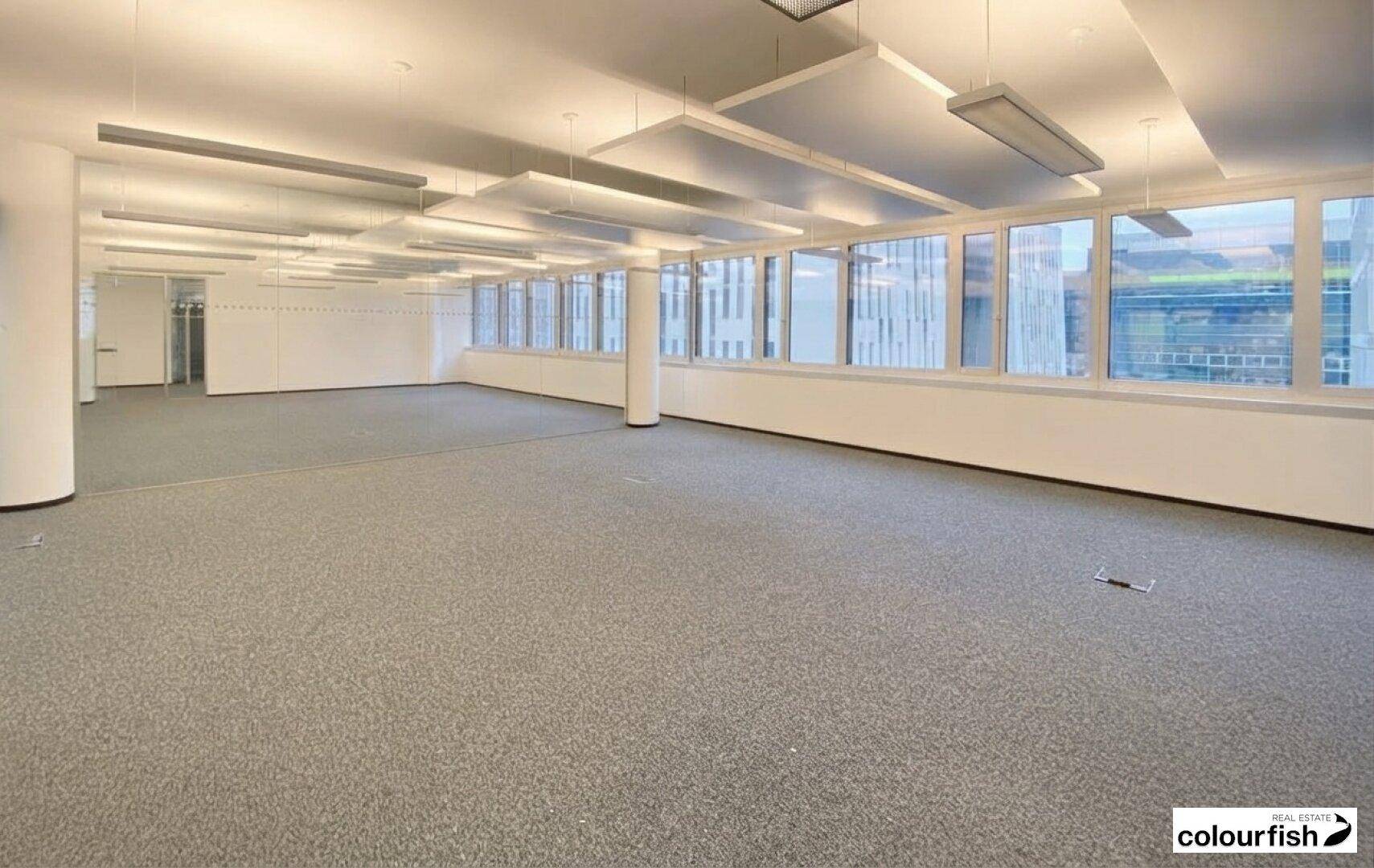 Helles Großraumbüro mit moderner Deckenbeleuchtung und weitem Blick auf die Stadt.