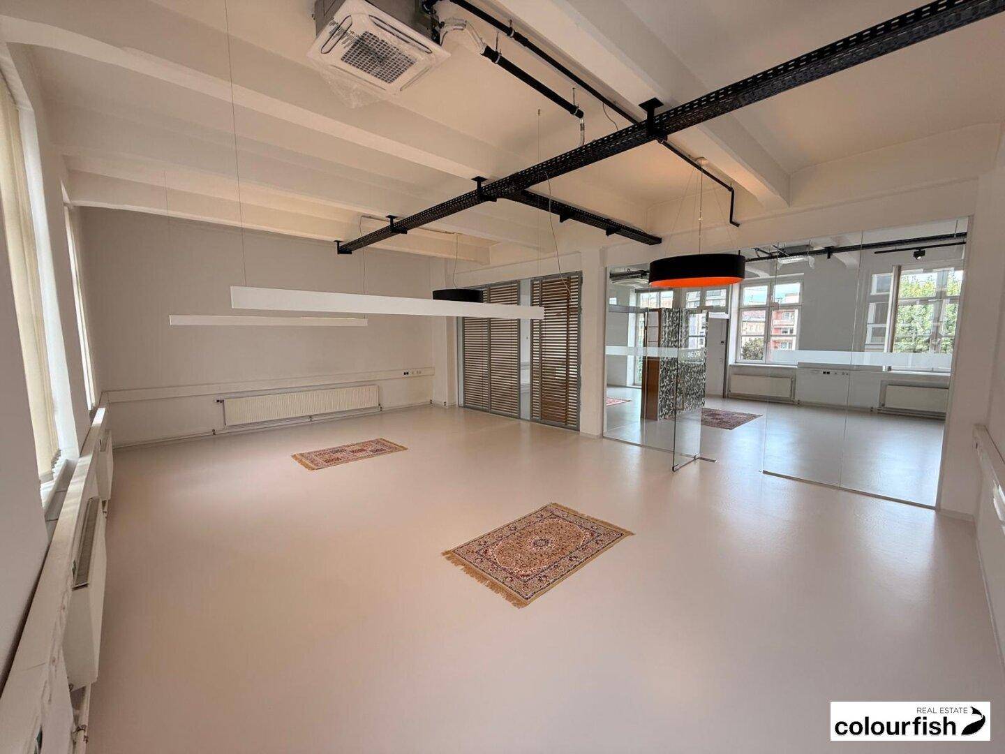 Weitläufiger Bürobereich mit modernen Glasabtrennungen und dekorativen Teppichen auf hellem Boden.