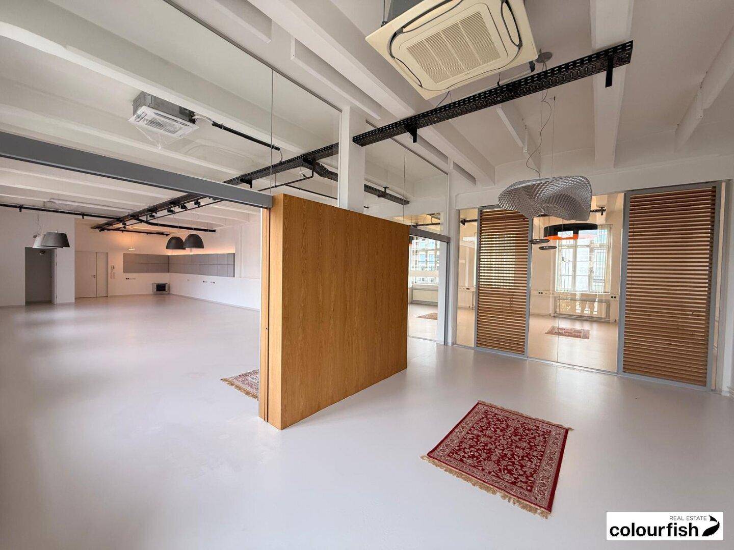 Geräumiger Bürobereich mit Holzwand, Glasabtrennungen und sichtbaren Deckeninstallationen.