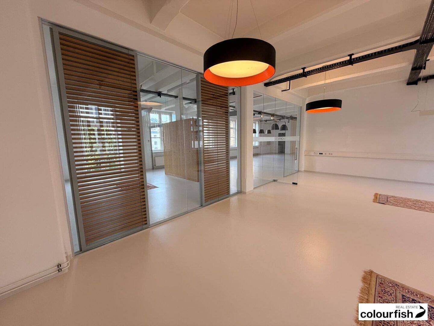 Moderner Büroraum mit Glas- und Holzlamellenwänden, sowie auffälligen Hängelampen.