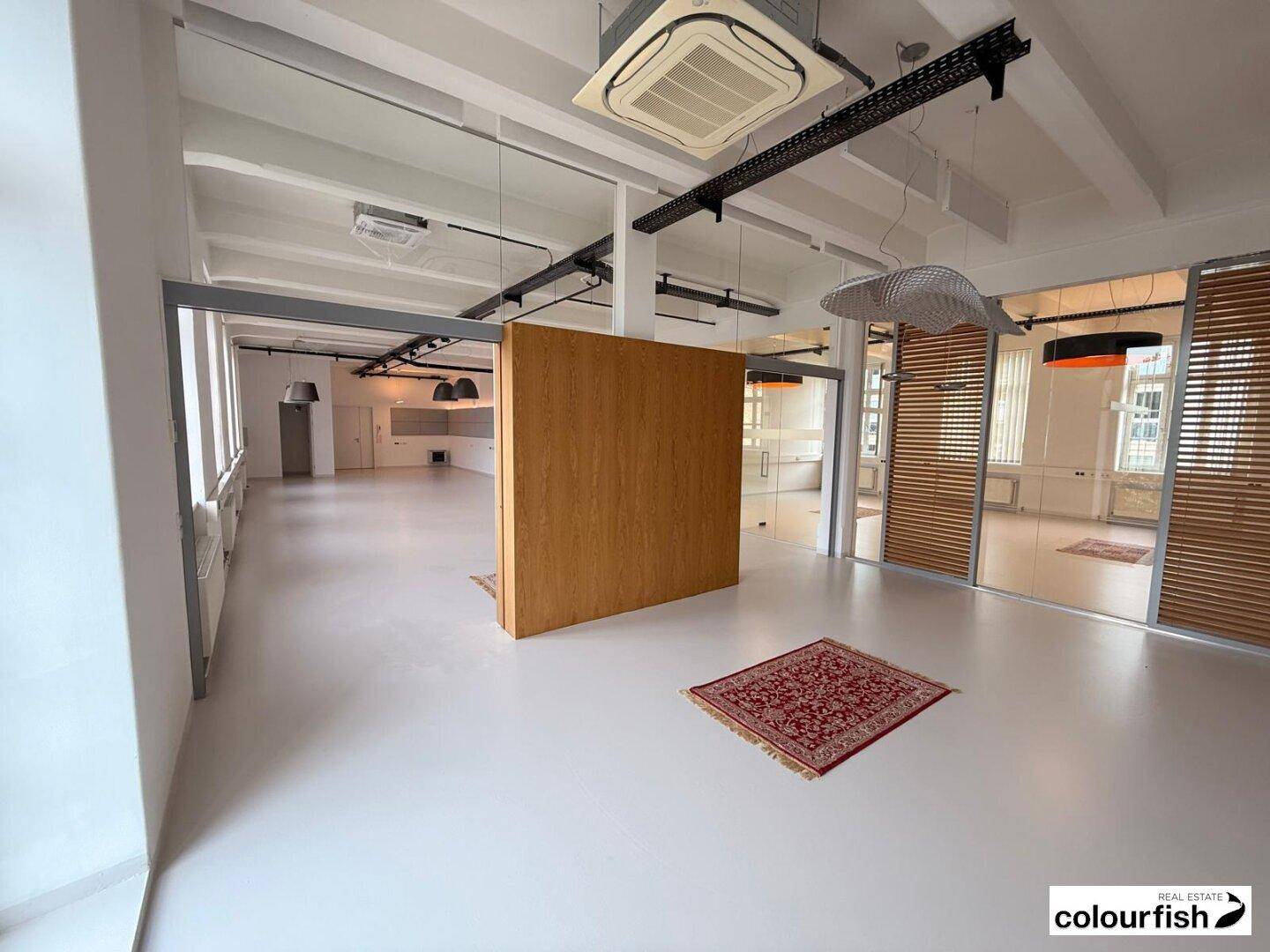 Weitläufiger Büroraum mit Holzelementen, Glaswänden und modernen Deckenleuchten.
