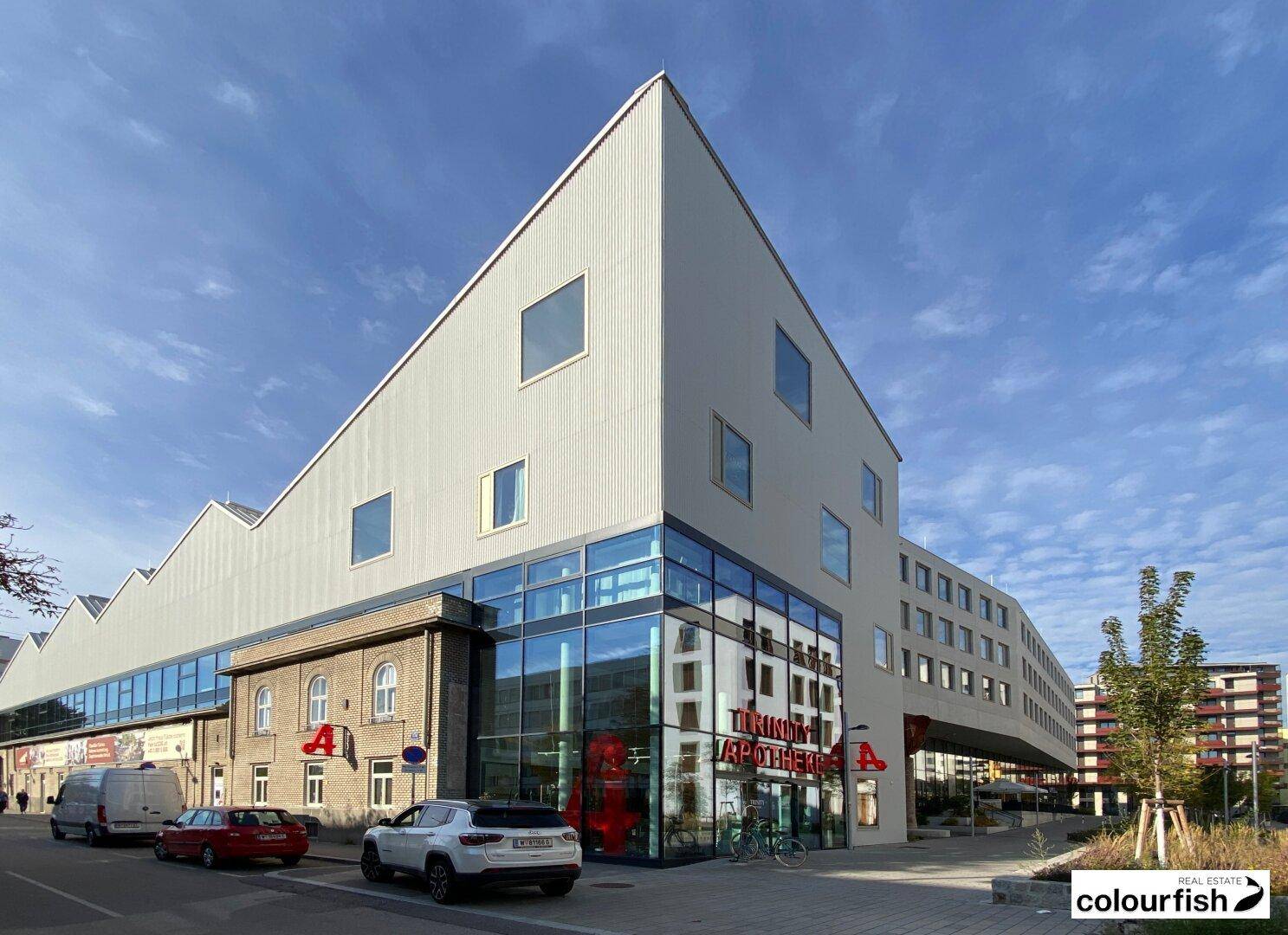 Markantes modernes Gebäude mit spitzem Dach und großer Glasfassade im Erdgeschoss, an einer belebten Straße gelegen.