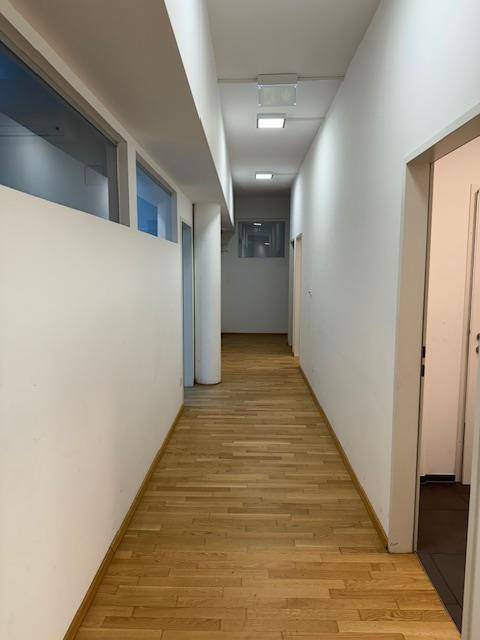 Langer, heller Flur mit Holzparkettboden, weißen Wänden und Deckenleuchten.