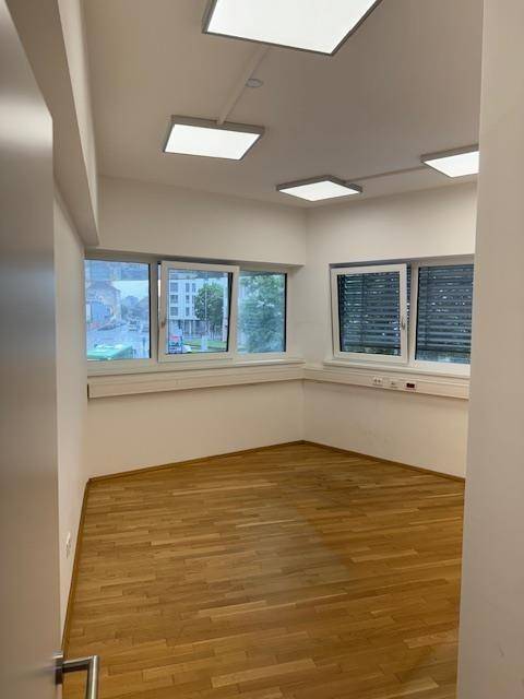 Eckbüro mit Holzparkettboden, zwei Fenstern und modernen quadratischen Deckenleuchten.