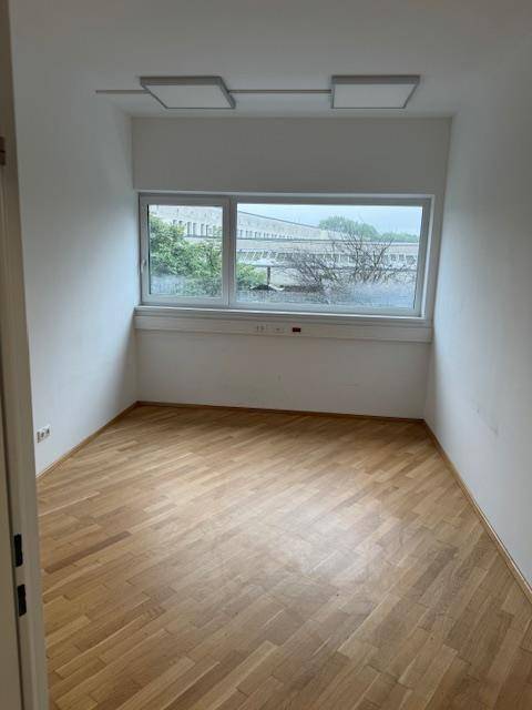 Kleiner Büroraum mit Holzparkettboden, einem großen Fenster und zwei Deckenleuchten.