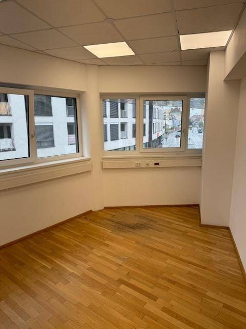 Büroraum mit Holzparkettboden, mehreren Fenstern und Blick auf die umliegenden Gebäude.