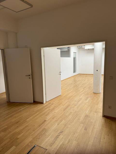 Offener Bürobereich mit Holzparkettboden, weißen Wänden und mehreren Türen.