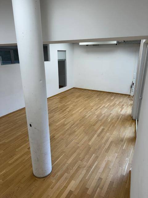 Geräumiger Büroraum mit Holzparkettboden, einer Säule und hohen Decken.