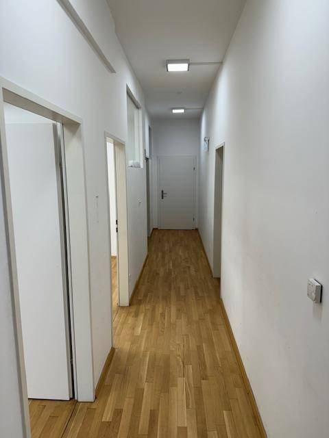 Langer, heller Flur mit Holzparkettboden, weißen Wänden und mehreren Türen.