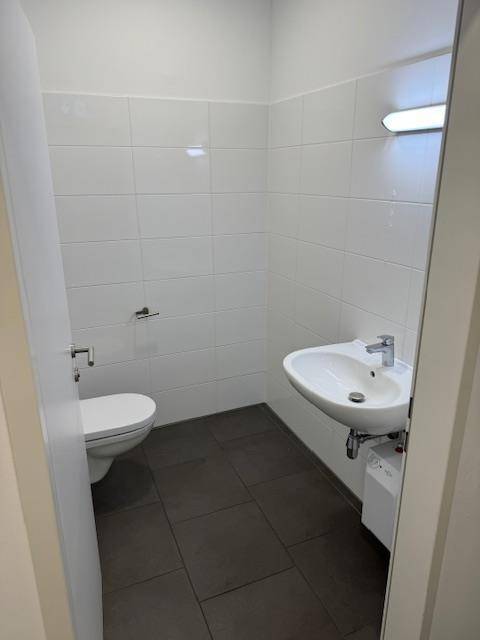 Moderne Gästetoilette mit weißen Fliesen, dunklem Boden und einem Waschbecken.