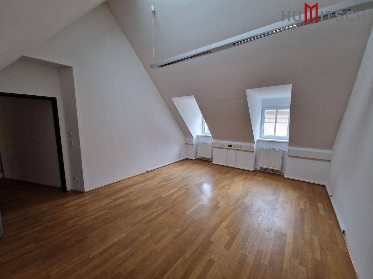 Dachgeschossbüro mit schrägen Wänden, Holzparkettboden und Dachfenstern, die eine helle Atmosphäre schaffen.