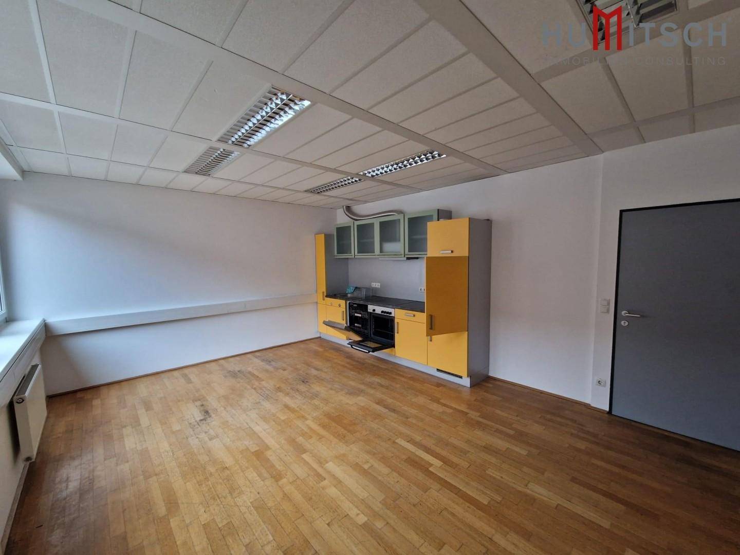 Bürofläche mit integrierter Küchenzeile, Holzparkettboden und Rasterdecke, ideal für Pausen und Verpflegung.