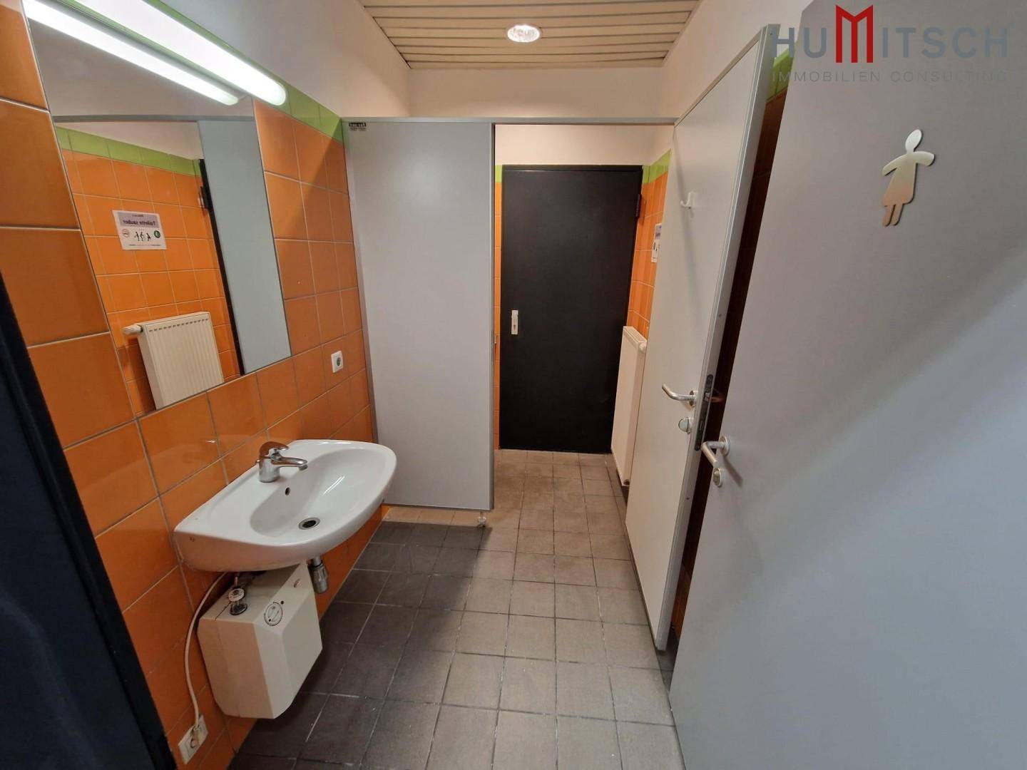 Sanitärbereich mit Waschbecken, Spiegel und orangefarbenen Fliesen, gut gepflegt und funktional ausgestattet.