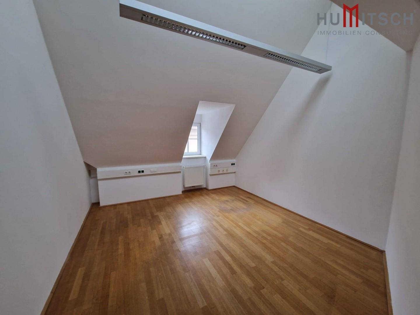 Dachgeschossbüro mit Holzparkettboden, schrägen Wänden und moderner Deckenbeleuchtung, in gutem Zustand.