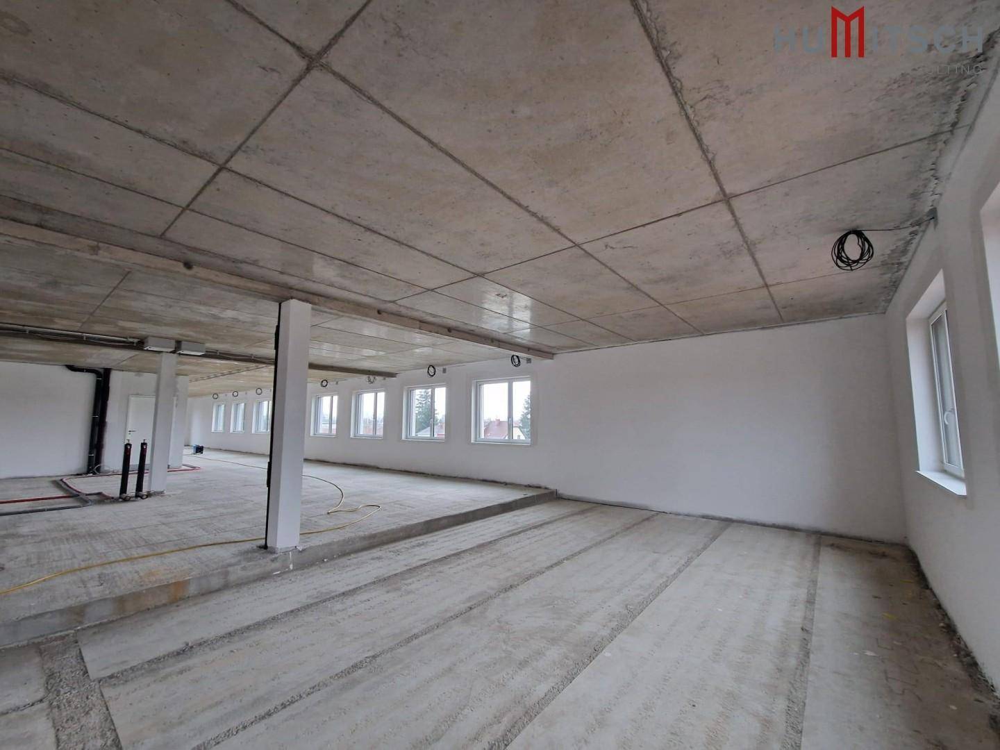 Rohbau eines Büroraums mit Betonboden, erhöhter Fläche und sichtbaren Installationen.