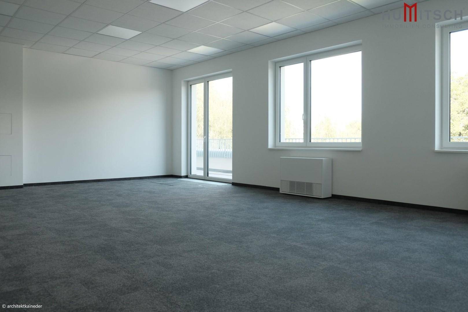 Heller Büroraum mit großem Schiebefenster und Teppichboden, möglicherweise mit Zugang zu einem Außenbereich.