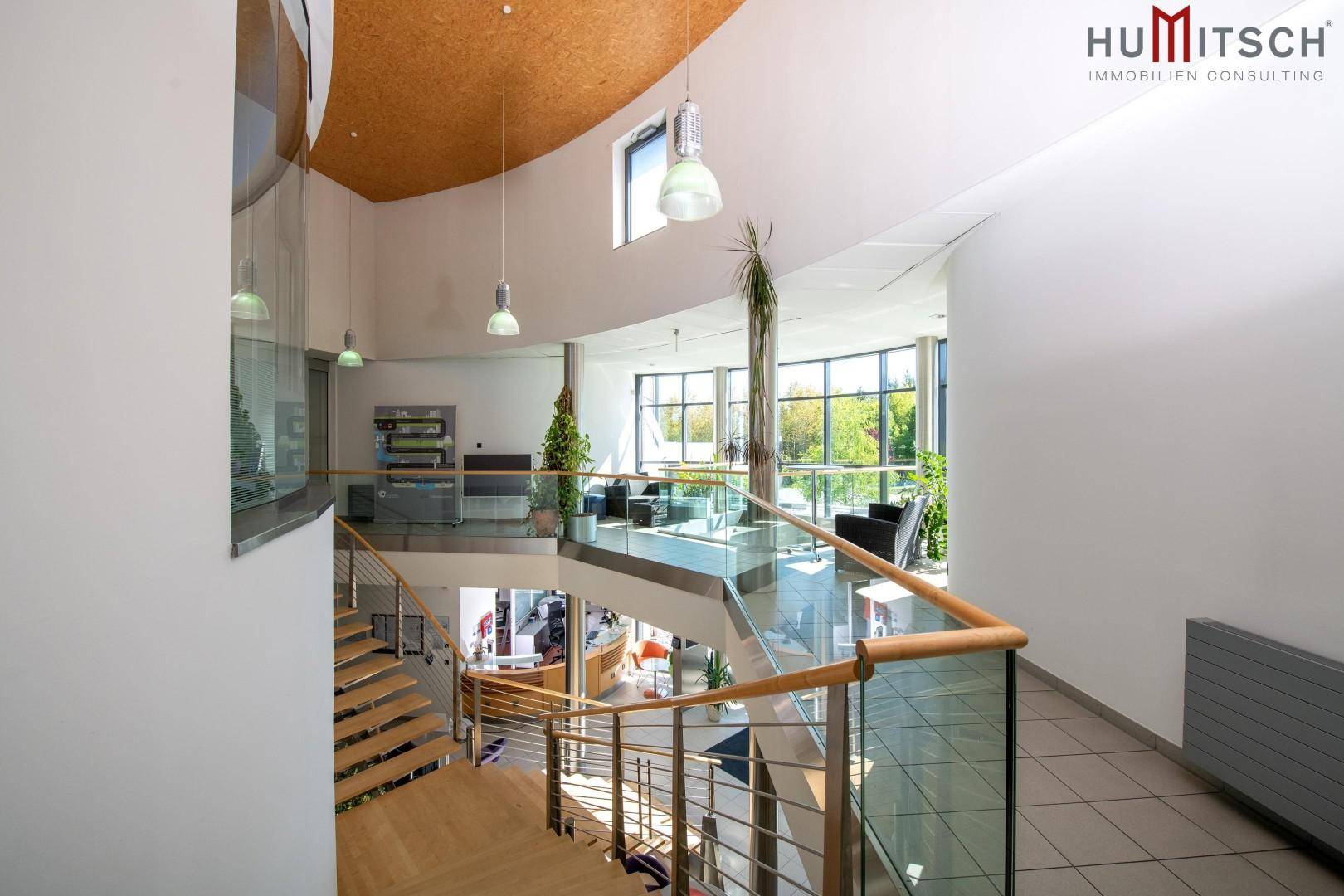 Modernes Treppenhaus mit Glasgeländer, Holzstufen und Blick auf den Empfangsbereich.