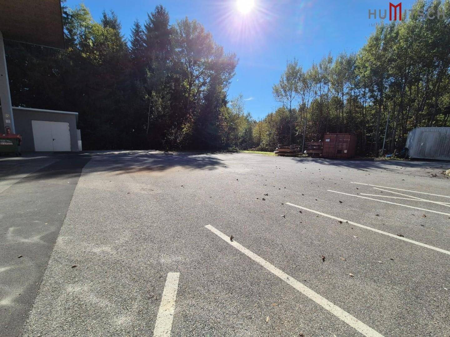 Großer Parkplatz mit Markierungen und umgebenden Bäumen unter strahlendem Sonnenschein.