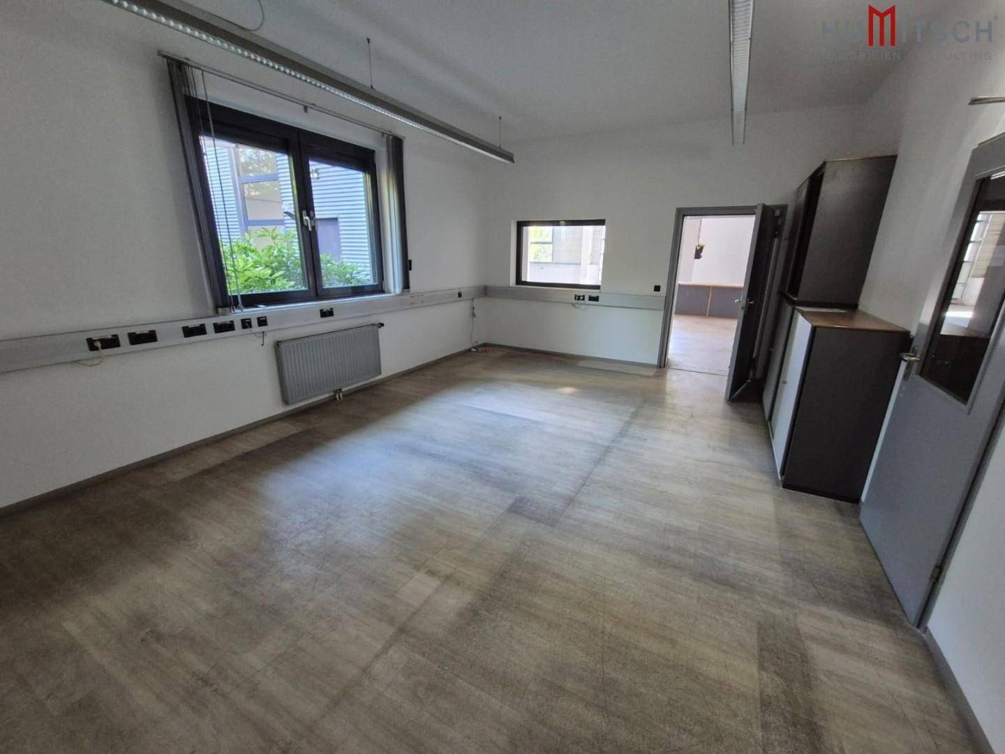 Geräumiges Büro mit Laminatboden, Fenstern und Blick ins Grüne.