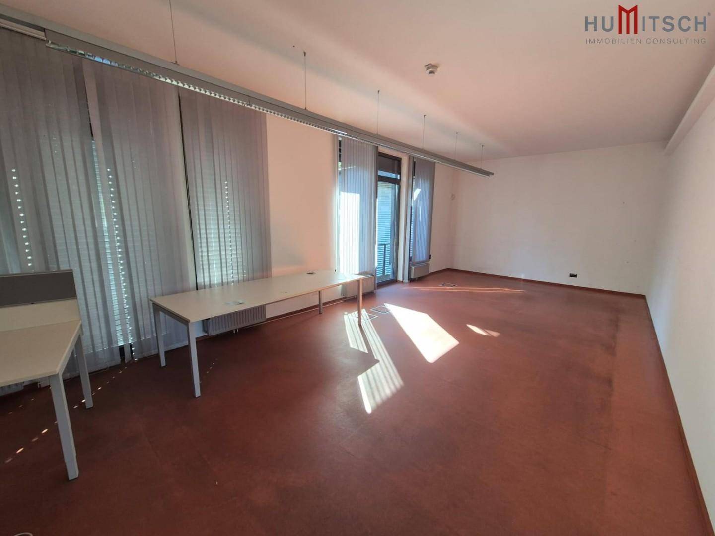 Bürofläche mit rotem Linoleumboden, großen Fenstern und viel Tageslicht.