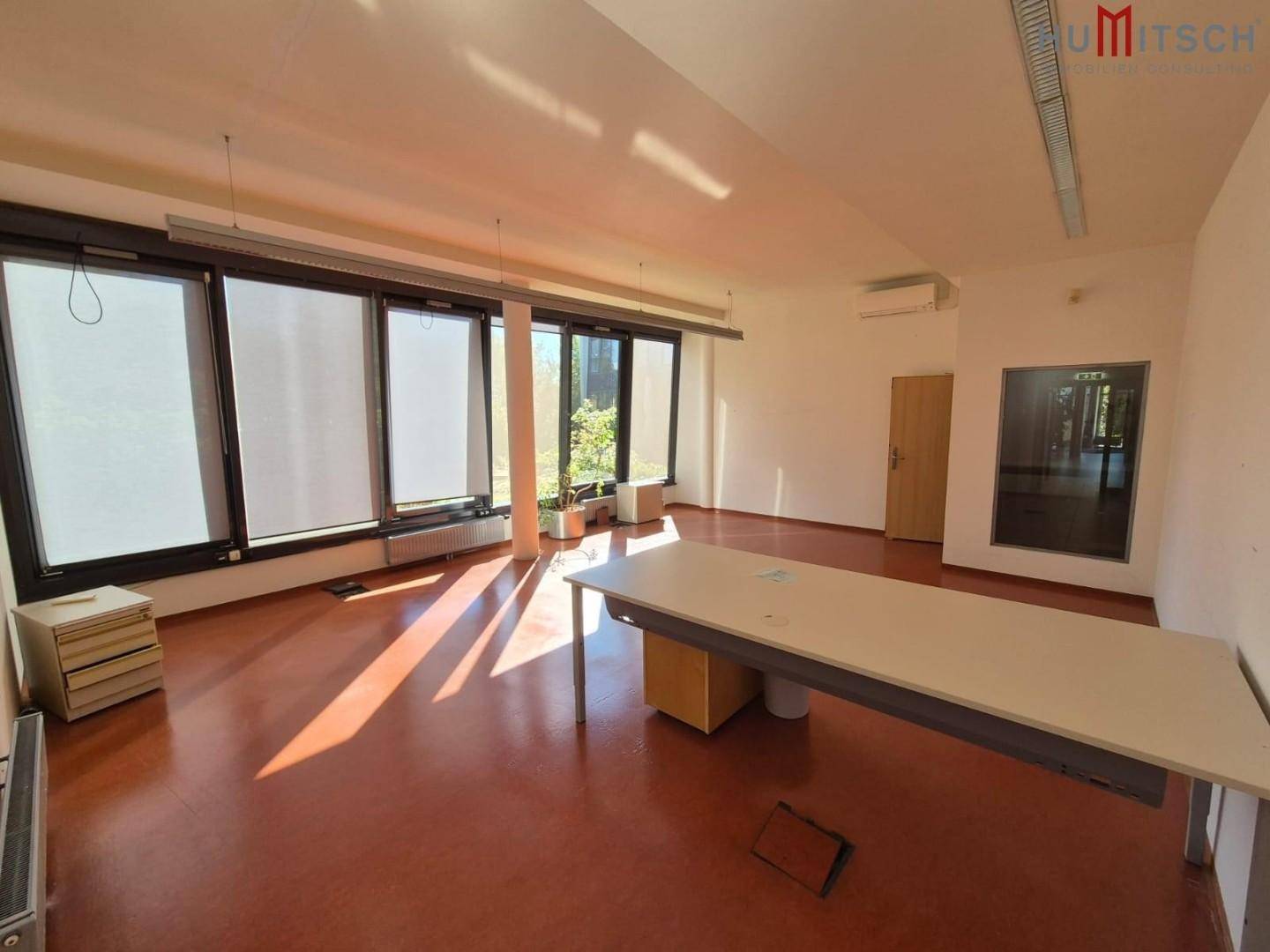 Großes Büro mit rotem Linoleumboden, Schreibtisch und großen Fenstern.