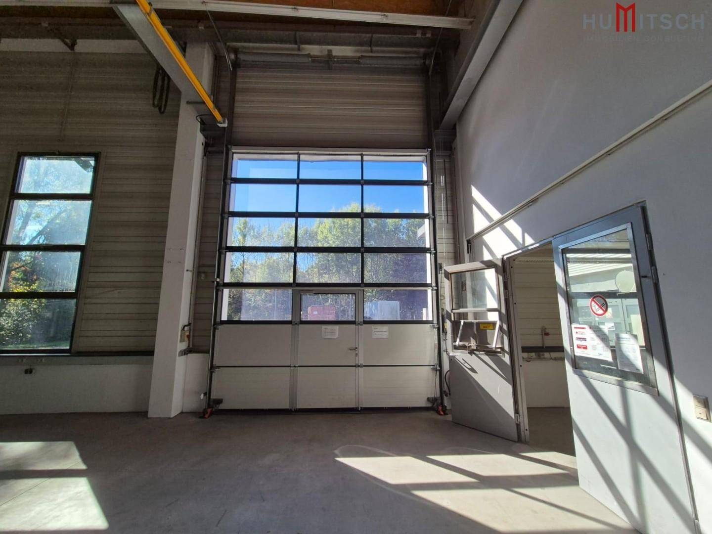 Große Lagerhalle mit Rolltor, separater Tür und hohen Fenstern.