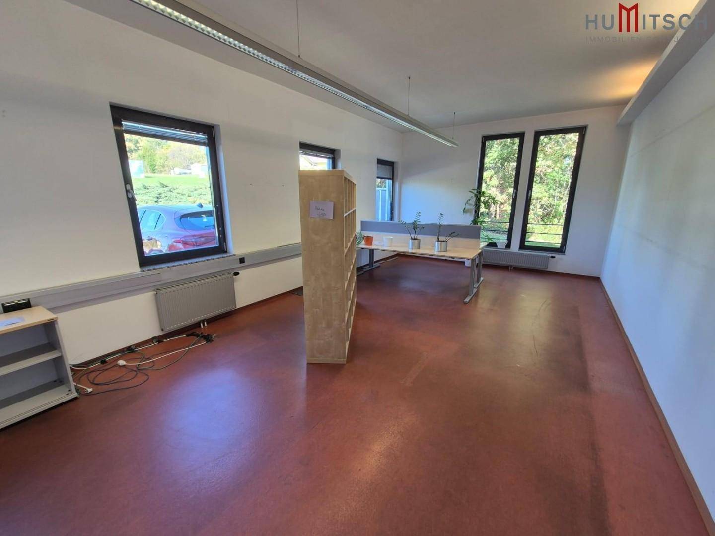 Büroraum mit rotem Vinylboden, Regalen und Fenstern mit Blick ins Grüne.