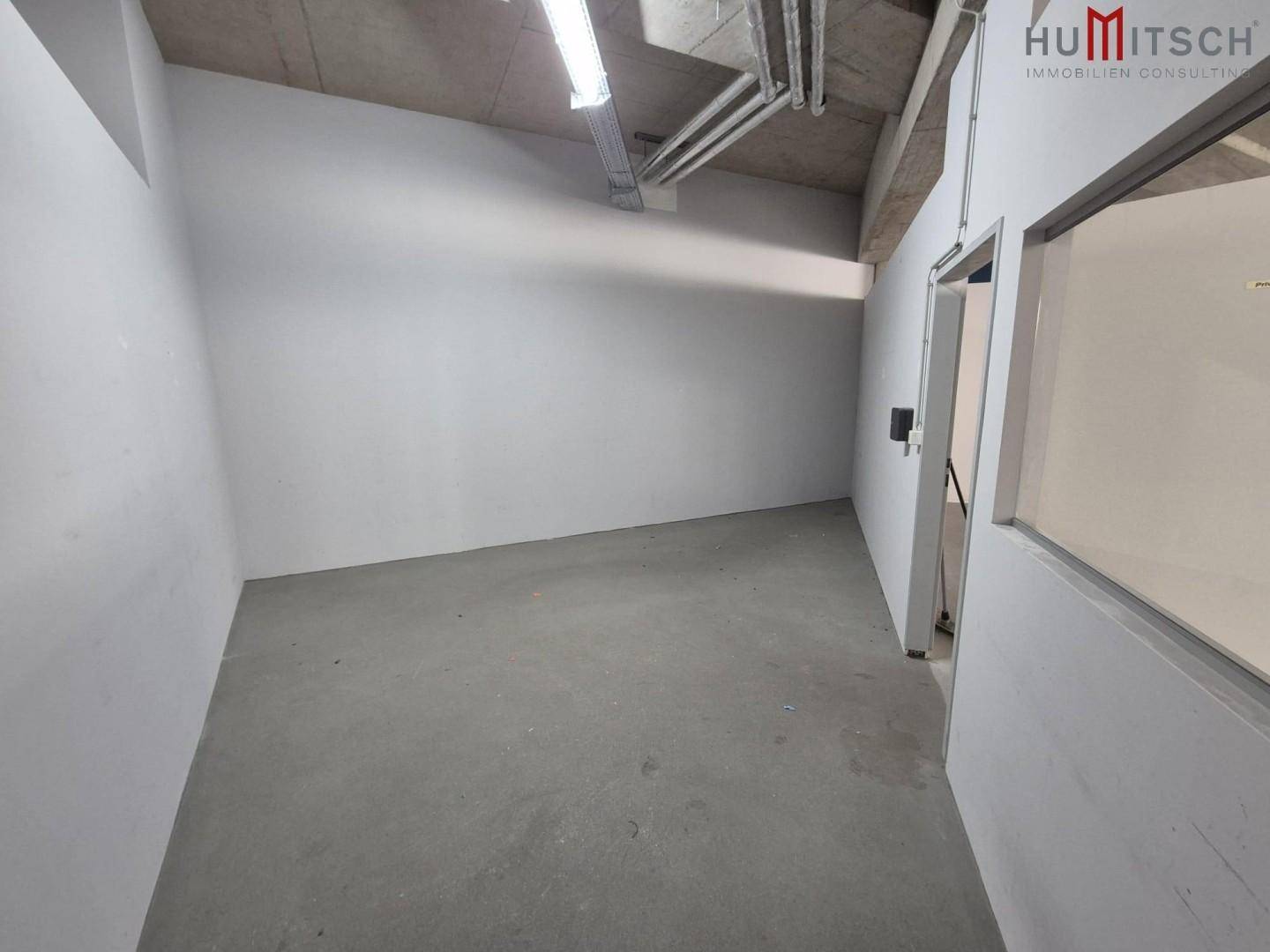 Kleiner, heller Raum mit Betonboden und weißen Wänden, ideal als Lager oder Büro.