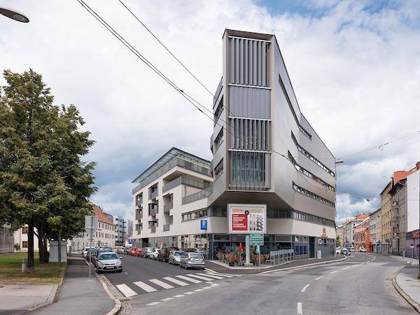 Modernes Gebäude an einer Straßenecke mit markanter Architektur und Geschäften im Erdgeschoss.