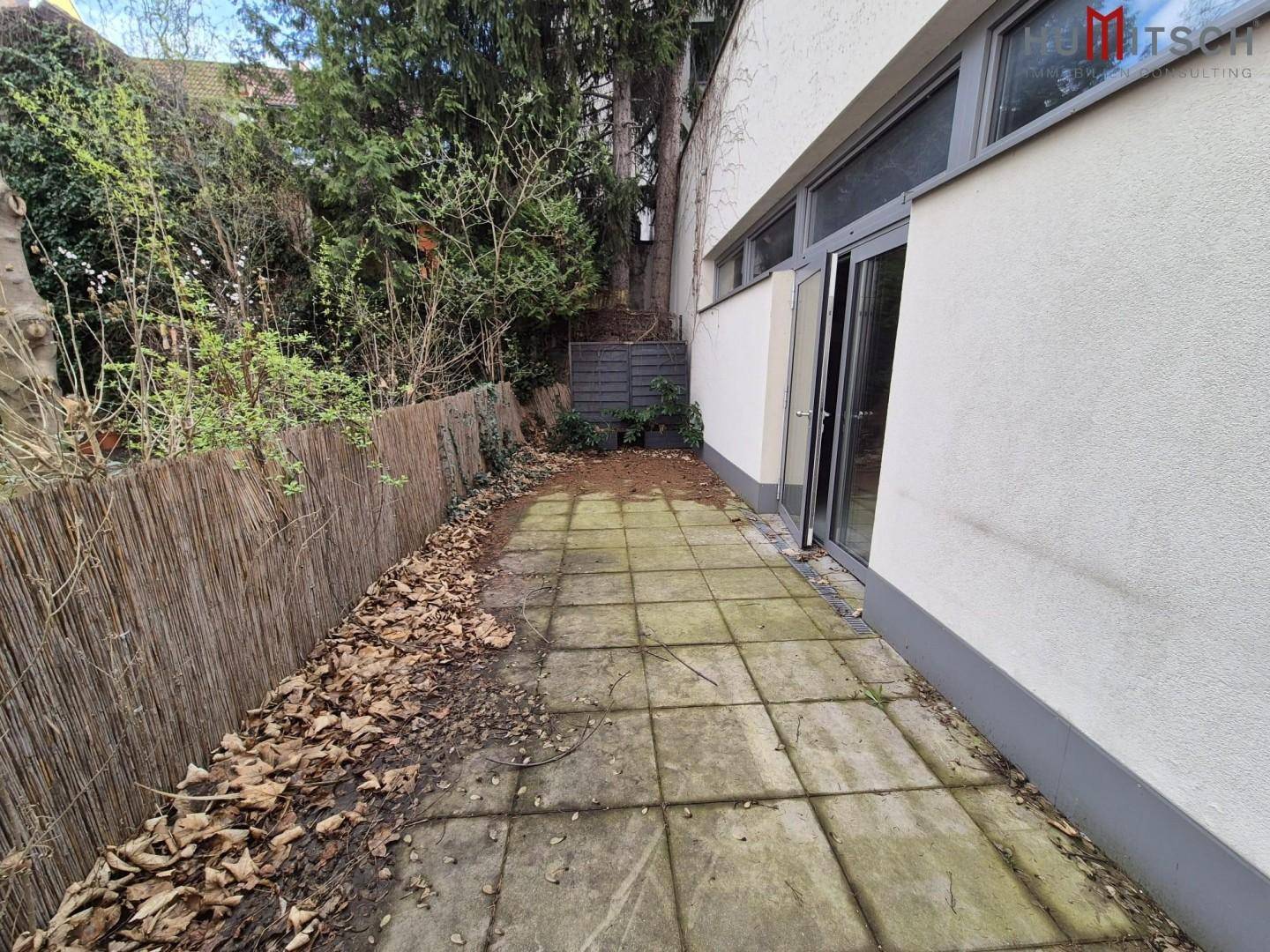 Kleine gepflasterte Terrasse mit Holzzaun und Bäumen, bietet einen privaten Außenbereich.