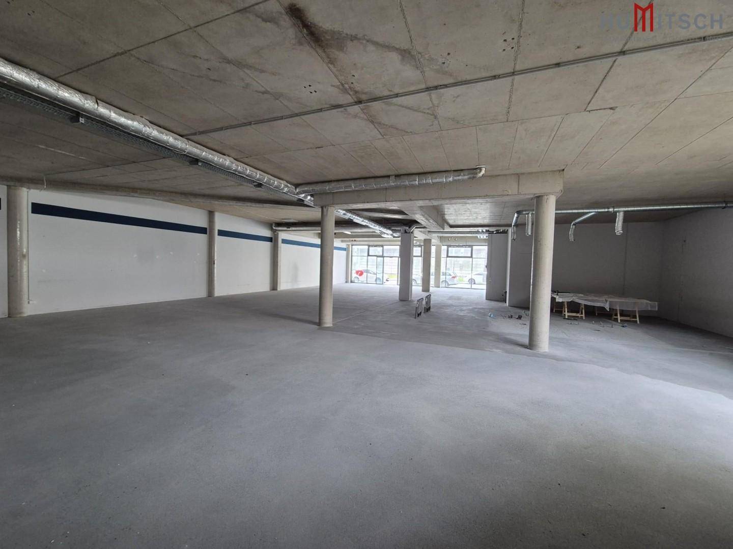 Geräumiger Gewerberaum mit Betonoberflächen und großen Fenstern, bereit für individuelle Gestaltung.