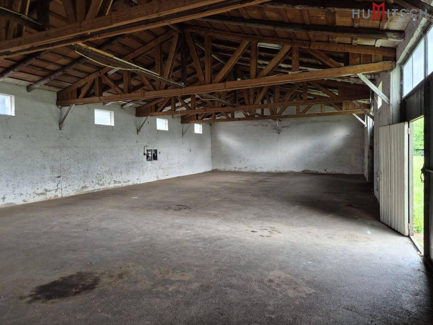 Große Lagerhalle mit Betonboden und sichtbarer Holzkonstruktion des Daches.