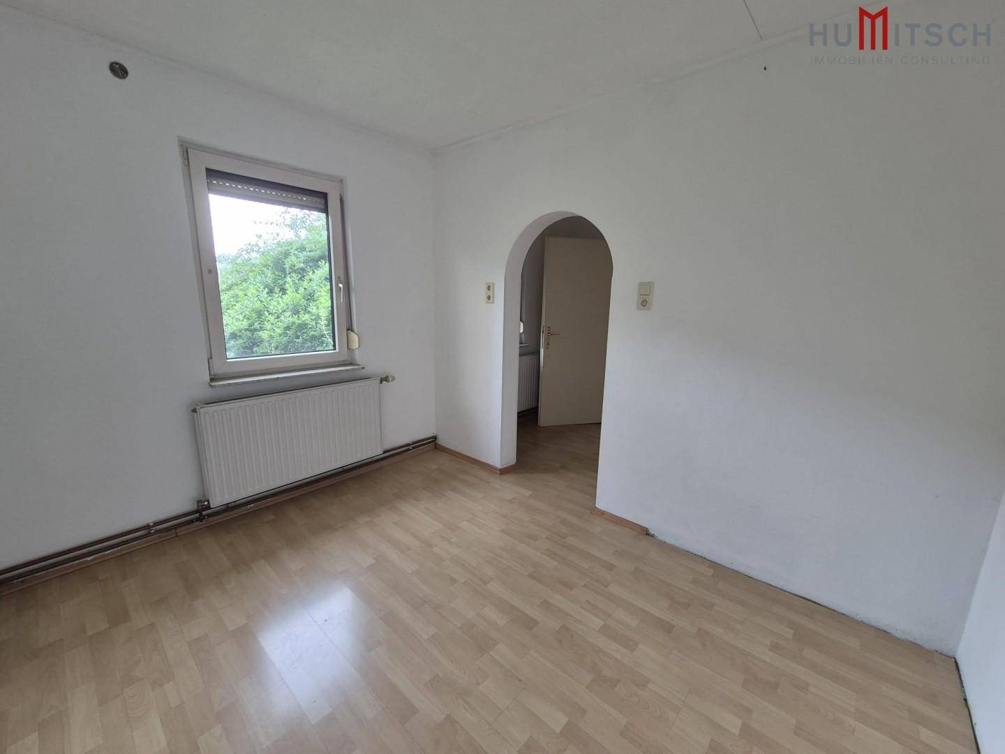 Unmöblierter Wohnraum mit Laminatboden, Fenster und einem Durchgang zu einem angrenzenden Zimmer.