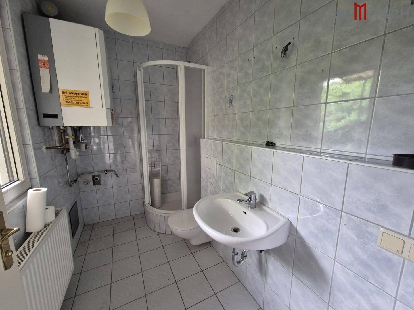 Gefliestes Badezimmer mit Duschkabine, Waschbecken und einem Fenster für natürliche Belüftung.