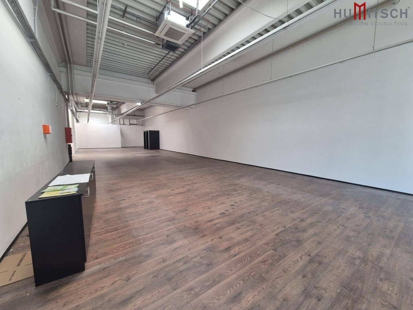 Geräumiger, leerstehender Gewerberaum mit Holzboden und hoher Decke, bereit für neue Mieter.