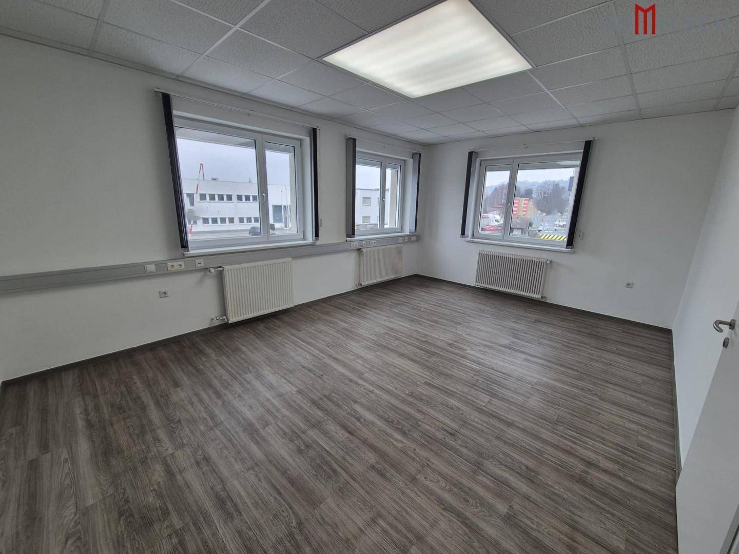 Geräumiges Büro mit Laminatboden, großen Fenstern und Deckenbeleuchtung, bereit zur Einrichtung.