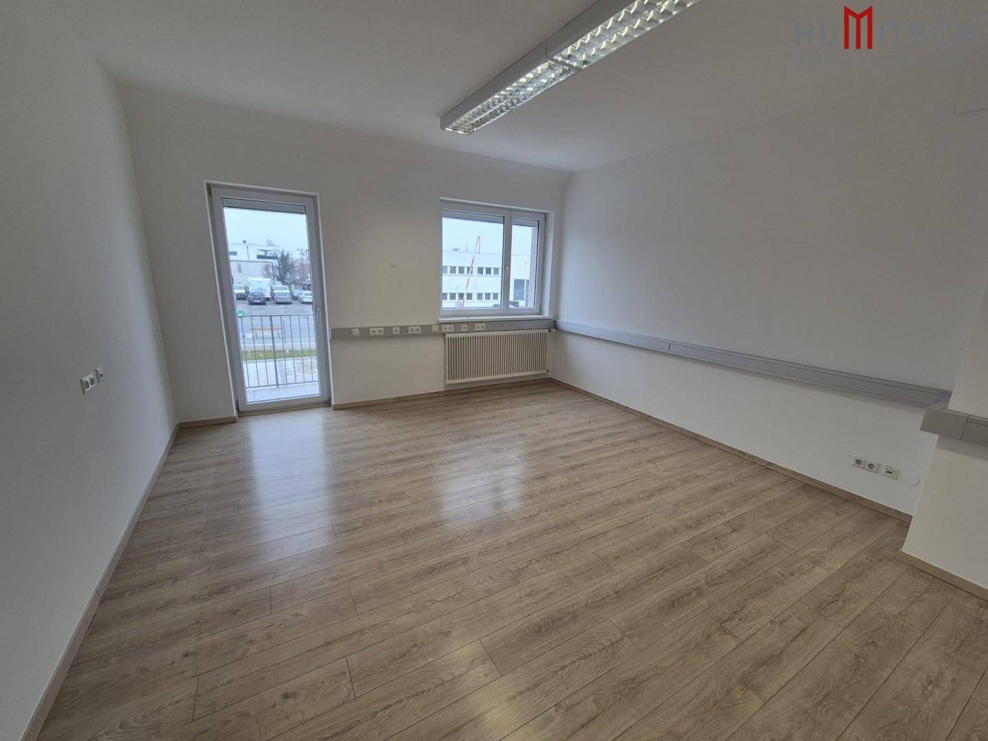 Büro mit Laminatboden, Fenster und Zugang zu einem Balkon, bietet viel Tageslicht.