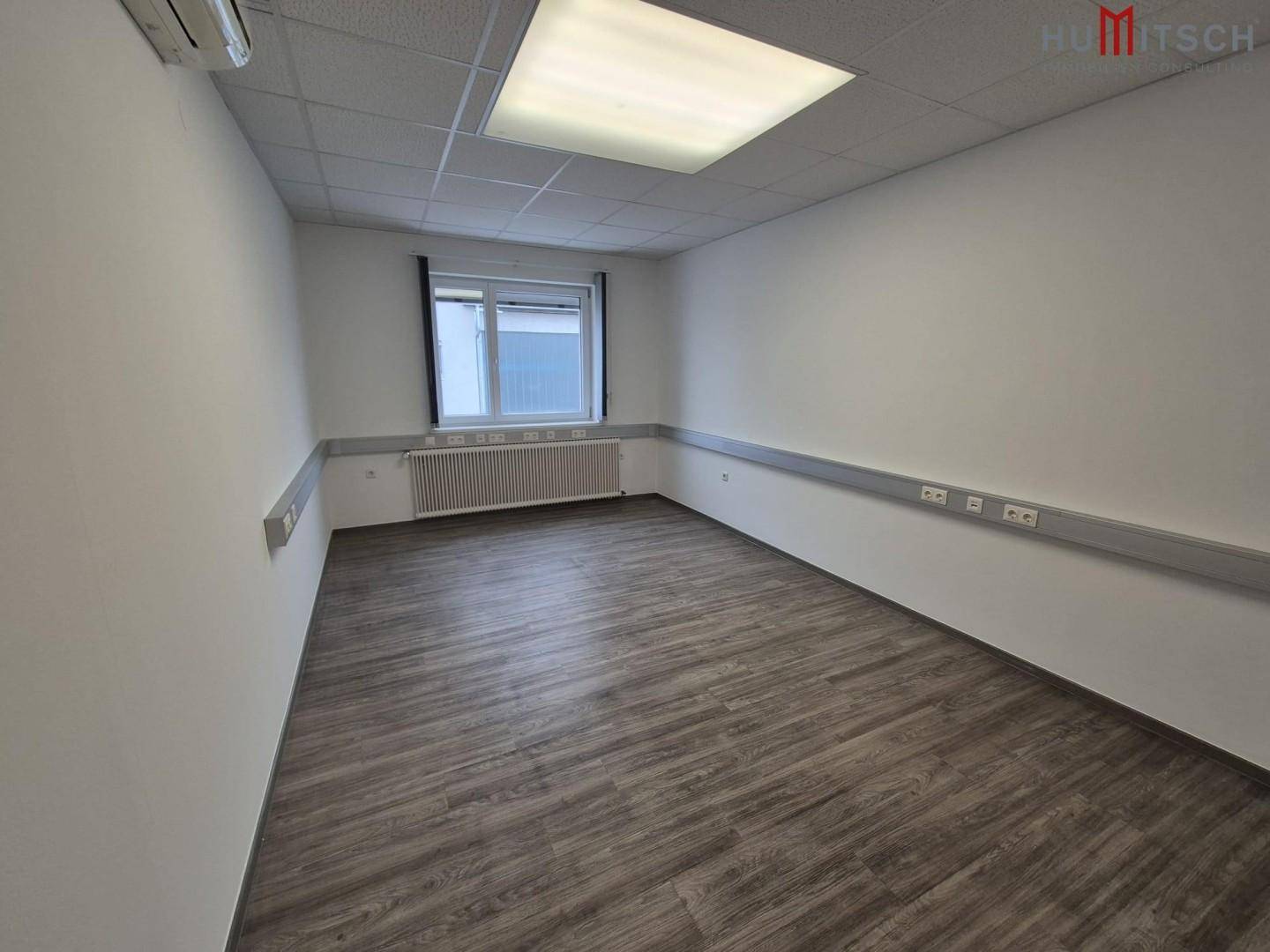 Büro mit Laminatboden, Fenster und Klimaanlage für angenehmes Raumklima und Komfort.