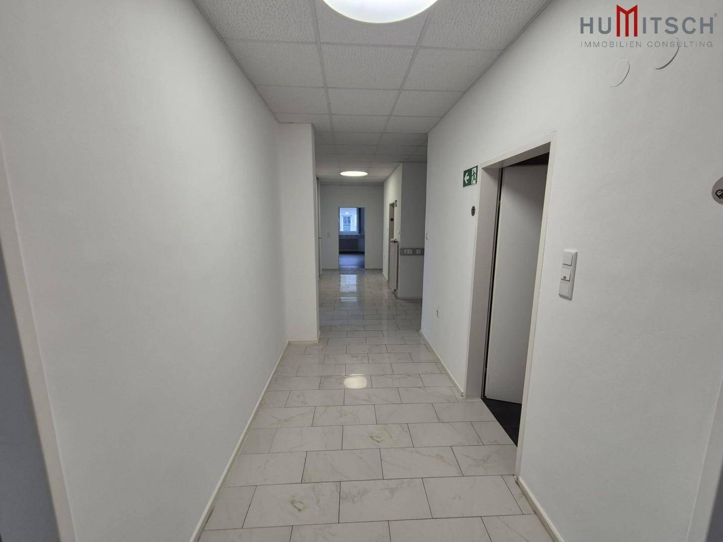 Heller Flur mit Fliesenboden und Zugang zu einem Aufzug, verbindet die verschiedenen Etagen.