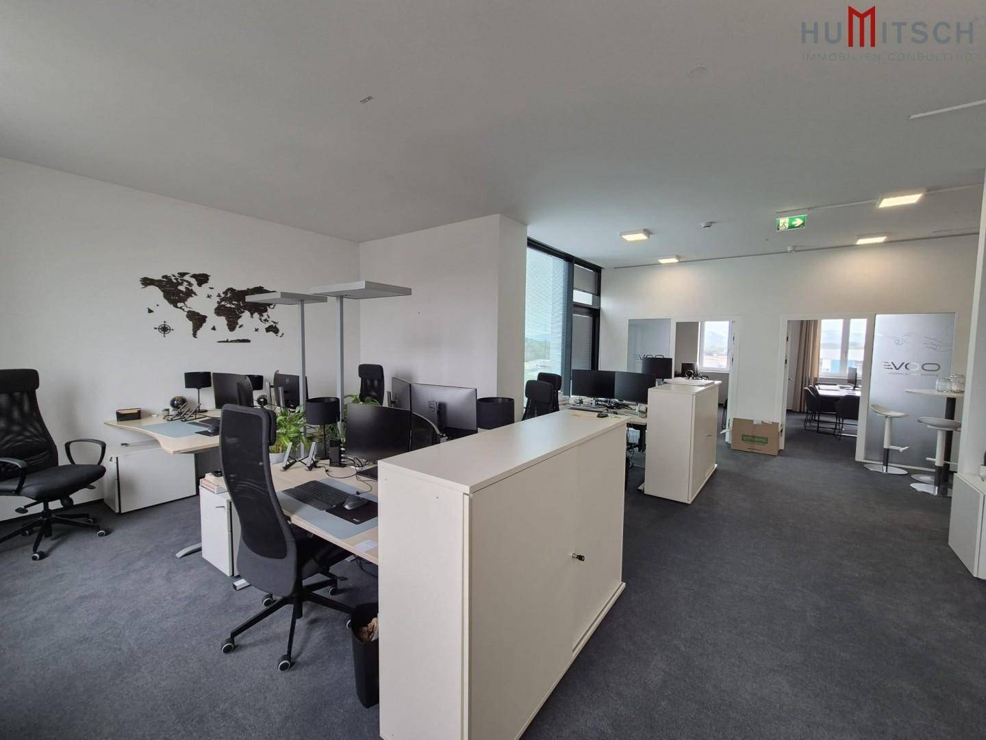 Offenes Büro mit mehreren Arbeitsplätzen, Weltkarten-Wanddekoration und Teppichboden.